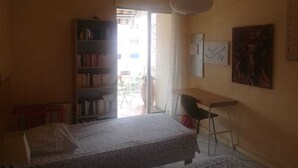 Un dormitorio con cama, escritorio, silla, estantería y ventana.