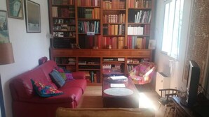 Un salón con un sofá rojo, un sillón amarillo, una estantería de madera y un televisor.