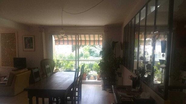 Un comedor con mesa y sillas, televisor y un balcón con plantas en macetas.