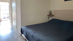 A bedroom with a bed, a nightstand with a lamp, a wall-mounted sign, and a door leading to a bright area.