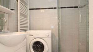 A modern bathroom with a built-in washing machine, a glass shower enclosure, and a white sink.