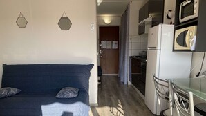 A compact living space with a sofa, a dining table, and a kitchen area including a microwave and refrigerator.