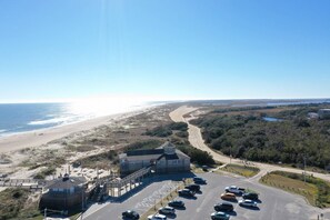 A coastal building with a parking lot and beach view. - Tipsea Toes - Private Home w/Backyard Oasis - Pool, Deck, Fire Pit, Close to Beach (Carolina Beach)