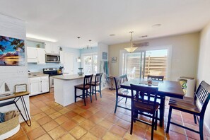 Una cocina con alacenas blancas, un microondas y una zona de comedor con sillas y una mesa de madera.
