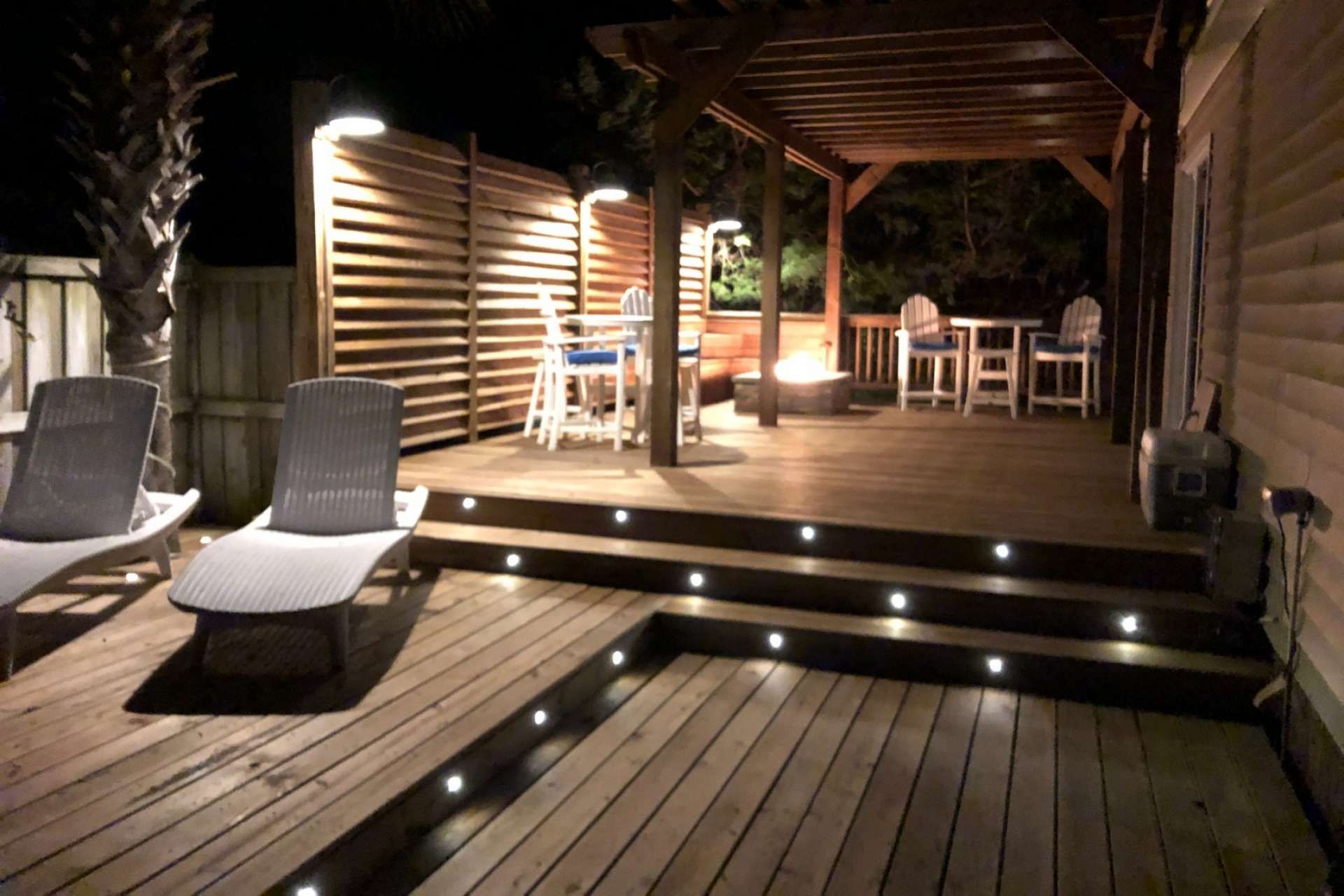 Een terras buiten met houten vloer, een overdekte zithoek met stoelen en tafels, en een klein zwembad.