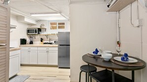 A modern kitchen with white cabinets, a microwave, and a refrigerator. There is a dining area with a table set for two, featuring plates, glasses, and a wine glass. - CUTE Studio | Newly Remodeled | Blocks To Downtown (Boise)