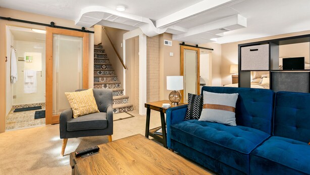 A modern living room with a blue sofa, a wooden coffee table, and a grey armchair. A staircase with patterned tiles leads to another room. - CUTE Studio | Newly Remodeled | Blocks To Downtown (Boise)