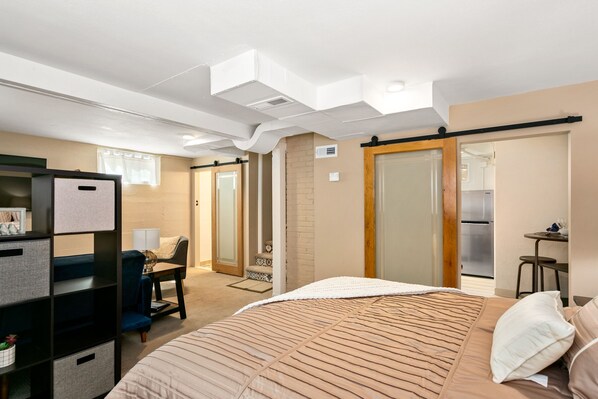 A bedroom with a bed, a desk, a chair, a wardrobe, and a small kitchenette area.