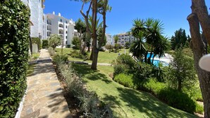 A pathway leading to a pool area surrounded by lush greenery and white buildings with balconies. - 51 - Apartment in Riviera walking distance to everything (Mijas Costa)