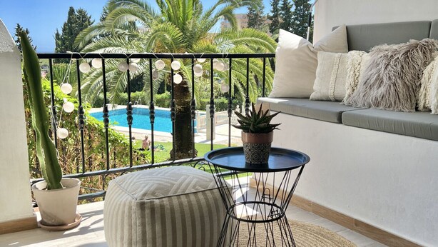 A balcony with a view of a pool, a potted plant, a round table, and a cushioned bench. - 51 - Apartment in Riviera walking distance to everything (Mijas Costa)