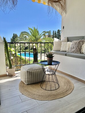 Een balkon met uitzicht op een zwembad, een plant in een pot, een ronde tafel en een comfortabele bank.