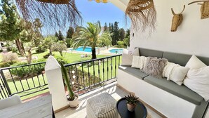 A balcony with a view of a pool, a sofa with cushions, a small table, and hanging decorations. - 51 - Apartment in Riviera walking distance to everything (Mijas Costa)