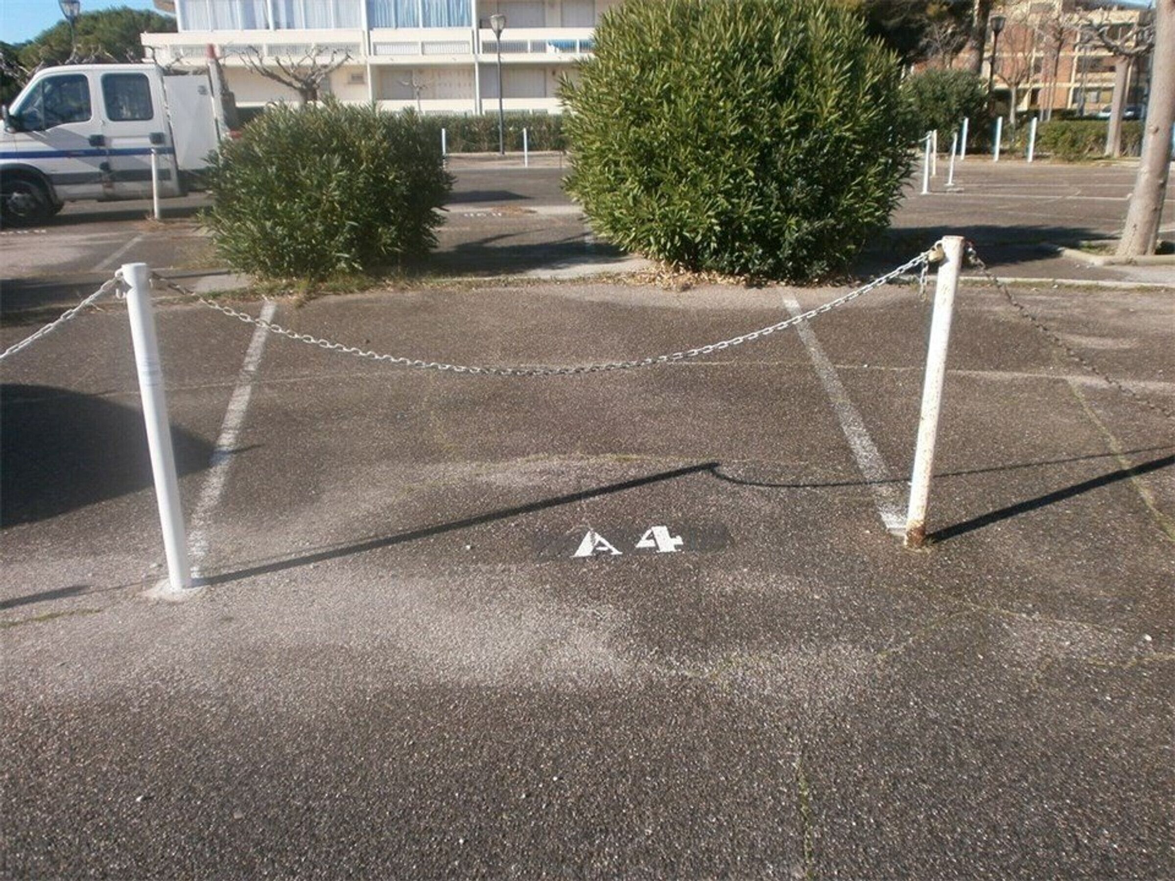 Ein Parkplatz mit einer Kettenbarriere, einem kleinen Busch und einem Gebäude im Hintergrund.