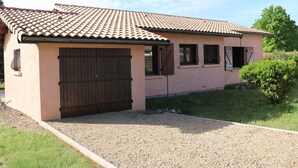 Een gelijkvloers huis met een pannendak, een grote houten garagedeur en een oprit met grind.