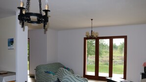 Een eetgedeelte met een tafel, stoelen en een kroonluchter. Er is een groot raam met uitzicht op groen.