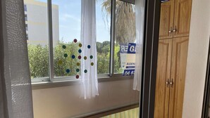 Ein Zimmer mit großem Fenster, einem Holzschrank und Blick auf Grünfläche.