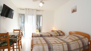 Ein Schlafzimmer mit zwei Betten, einem Schreibtisch mit Stühlen, einem Fernseher und einem Deckenventilator.