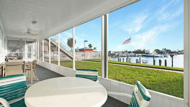 A covered patio with a white table and green chairs, overlooking a marina with boats and an American flag.
