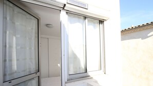 Een balkon met een witte reling, een schuifpui en een raam.
