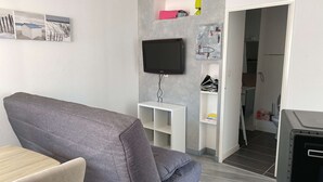 Een moderne woonkamer met een grijze bank, een flatscreen televisie aan de muur en een klein wit dressoir.