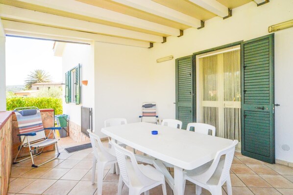 A patio with a white table and chairs, a striped chair, and a grill.