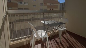 A balcony with a metal table and two white chairs, overlooking a residential building. - Cozy T1 in Balaruc-les-Bains with Balcony, A/C, and Modern Amenities (Balaruc-les-Bains)