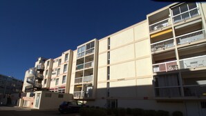 A multi-story residential building with balconies, a parking area, and a small garden. - Cozy T1 in Balaruc-les-Bains with Balcony, A/C, and Modern Amenities (Balaruc-les-Bains)