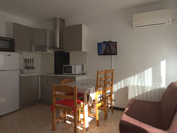 A compact kitchen with a dining table, chairs, a microwave, a stove, and an air conditioning unit.