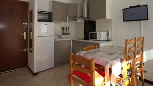 A compact kitchen with a microwave, toaster, and stove, a dining table with chairs, and a clock on the wall. - Cozy T1 in Balaruc-les-Bains with Balcony, A/C, and Modern Amenities (Balaruc-les-Bains)
