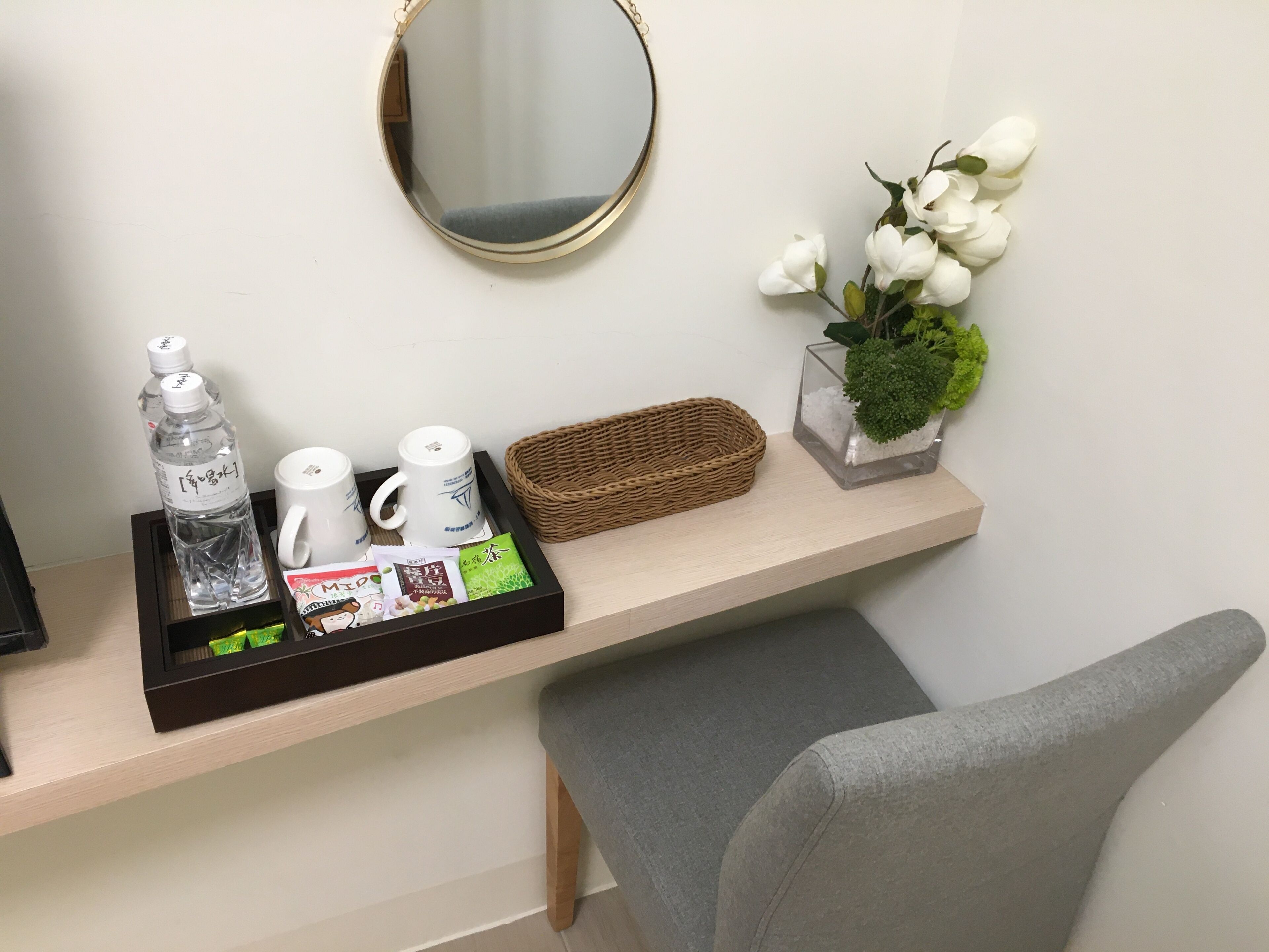 A hotel reception area with a wooden counter, a mirror, a tray with bottled water, tea cups, and a small potted plant.
