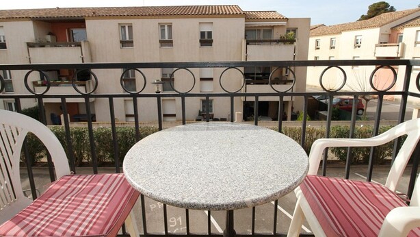 Ein Balkon mit einem runden Tisch, zwei Stühlen, einem Metallgeländer und Blick auf Wohnhäuser im Hintergrund.