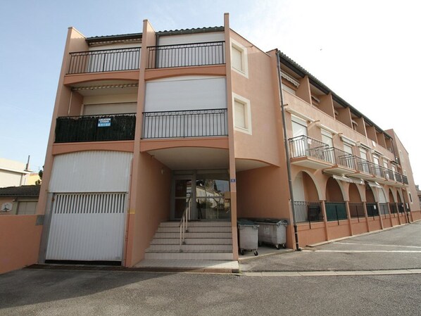 A multi-story residential building with balconies, a gated entrance, and a parking area.