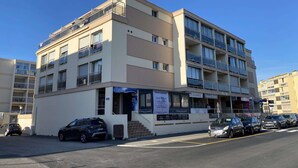 Un immeuble à plusieurs étages doté de balcons, avec une entrée au niveau du sol et plusieurs voitures garées.