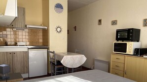 Une cuisine compacte équipée d’un réfrigérateur, d’un four à micro-ondes et d’un grille-pain. On y trouve une table à manger avec des chaises et une petite horloge au mur.