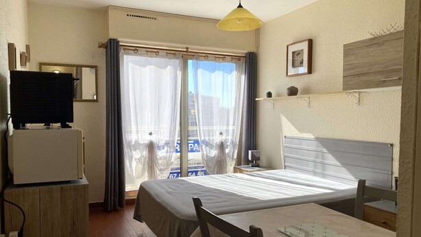 Une chambre d’hôtel comprenant un lit, un bureau avec une chaise, une télévision et une fenêtre avec des rideaux.