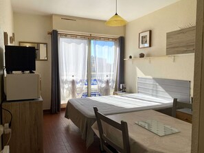 Een hotelkamer met een bed, een bureau met stoel, een televisie en een raam met gordijnen.