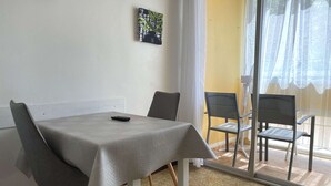 A dining area with a table and chairs, a remote control on the table, and a painting on the wall. - Bright studio with air conditioning and wifi in Balaruc-les-Bains (Balaruc-les-Bains)