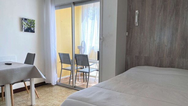 A hotel room with a bed, a table with chairs, a sliding glass door leading to a balcony, and a wooden wall. - Bright studio with air conditioning and wifi in Balaruc-les-Bains (Balaruc-les-Bains)