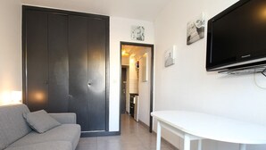 A modern living room with a grey sofa, a white table, and a flat-screen TV mounted on the wall. - Cozy Studio with Garden, Near Thermes, WiFi, AC (Balaruc-les-Bains)