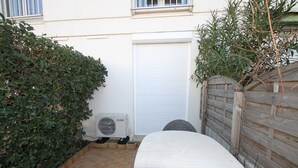 A patio with a table and chairs, a white garage door, and a wooden fence. - Cozy Studio with Garden, Near Thermes, WiFi, AC (Balaruc-les-Bains)