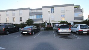 A parking lot with several cars, a building with multiple windows and balconies, and a street lamp. - Cozy Studio with Garden, Near Thermes, WiFi, AC (Balaruc-les-Bains)