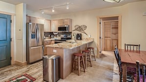 A modern kitchen with stainless steel appliances, a central island with stools, and a dining area with a wooden table and chairs. - Updated 2 Bedroom Walking Distance to the SuperBee Lift!! (Frisco)