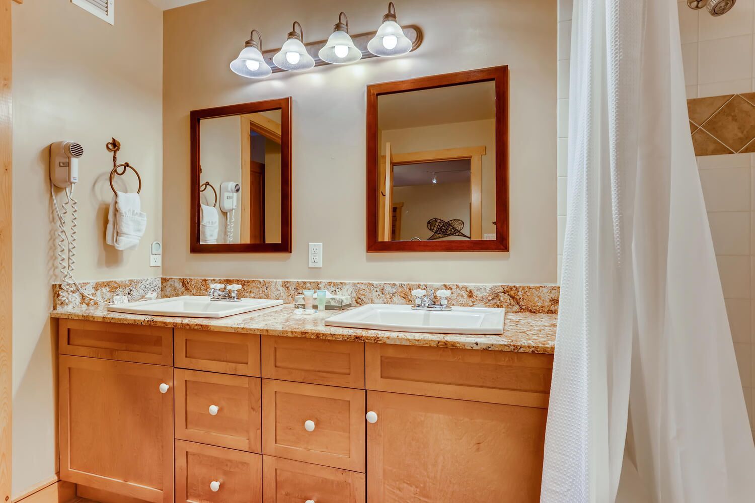 A bathroom with two sinks, wooden cabinets, and a mirror with lights above.