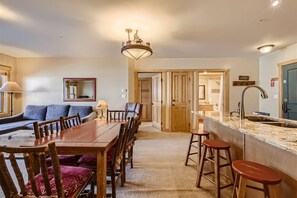 A spacious living area with a wooden dining table, a sofa, and a kitchen with a granite countertop and stools.