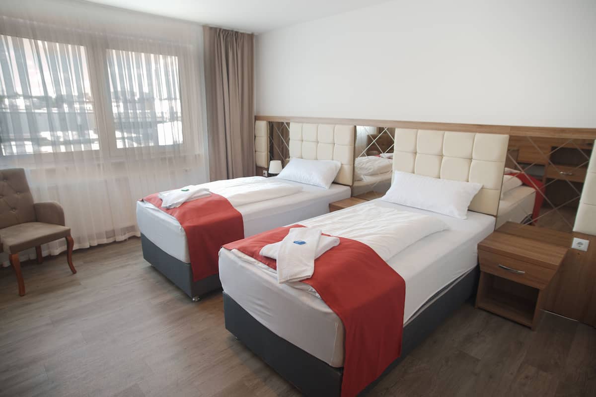 A hotel room with two beds, a wooden nightstand, a chair, and a large window with curtains.