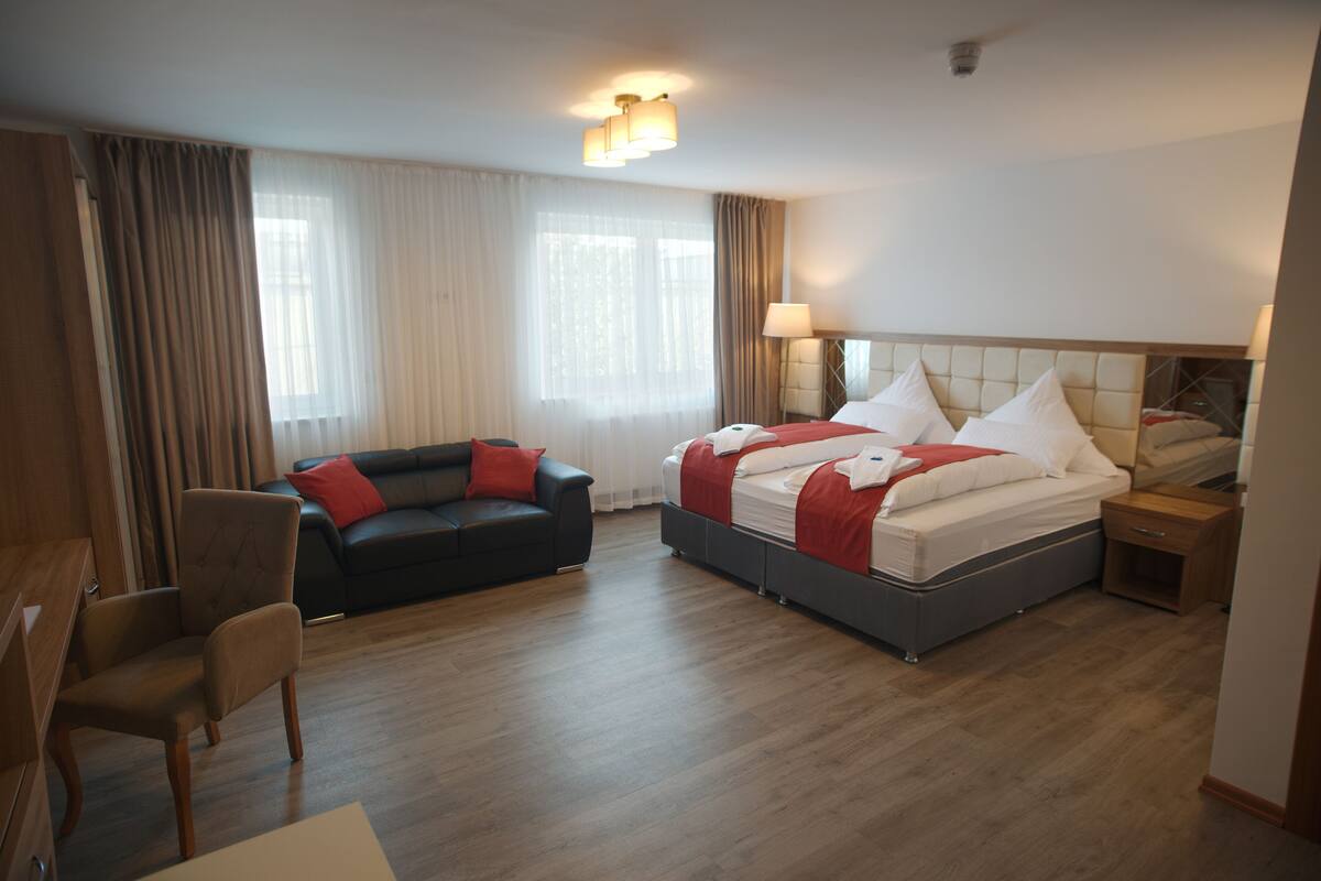 A hotel room with a bed, a sofa, a desk, and a chair.