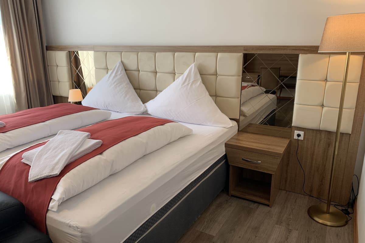 A hotel room with a large bed, a bedside table, a lamp, and a wooden floor.