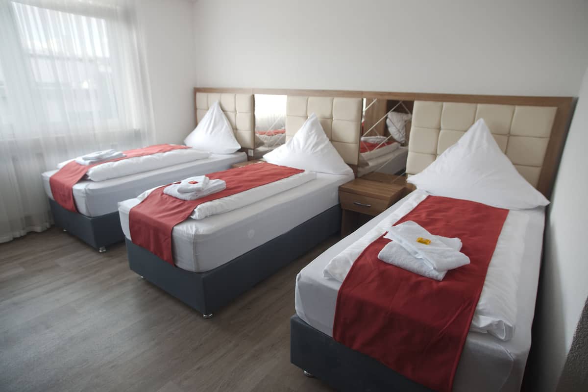 A hotel room with two beds, each with a red blanket and white pillows, a wooden nightstand, and a mirror above the beds.