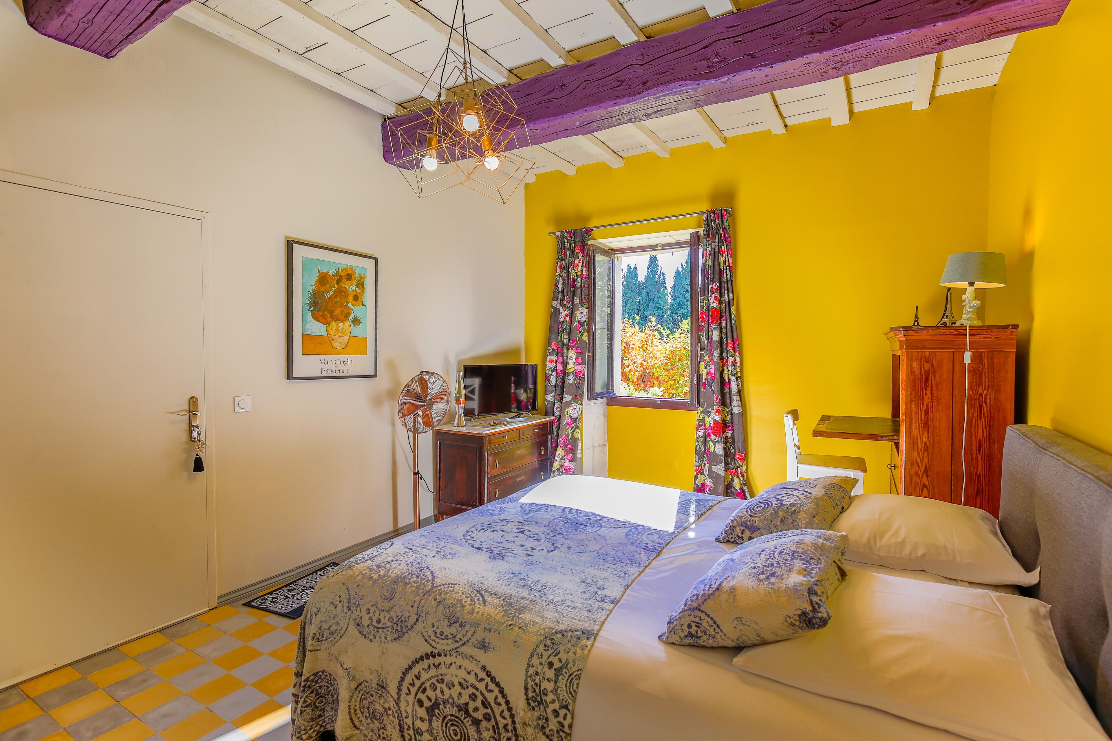 A bedroom with a bed, a dresser, a fan, and a window with curtains.