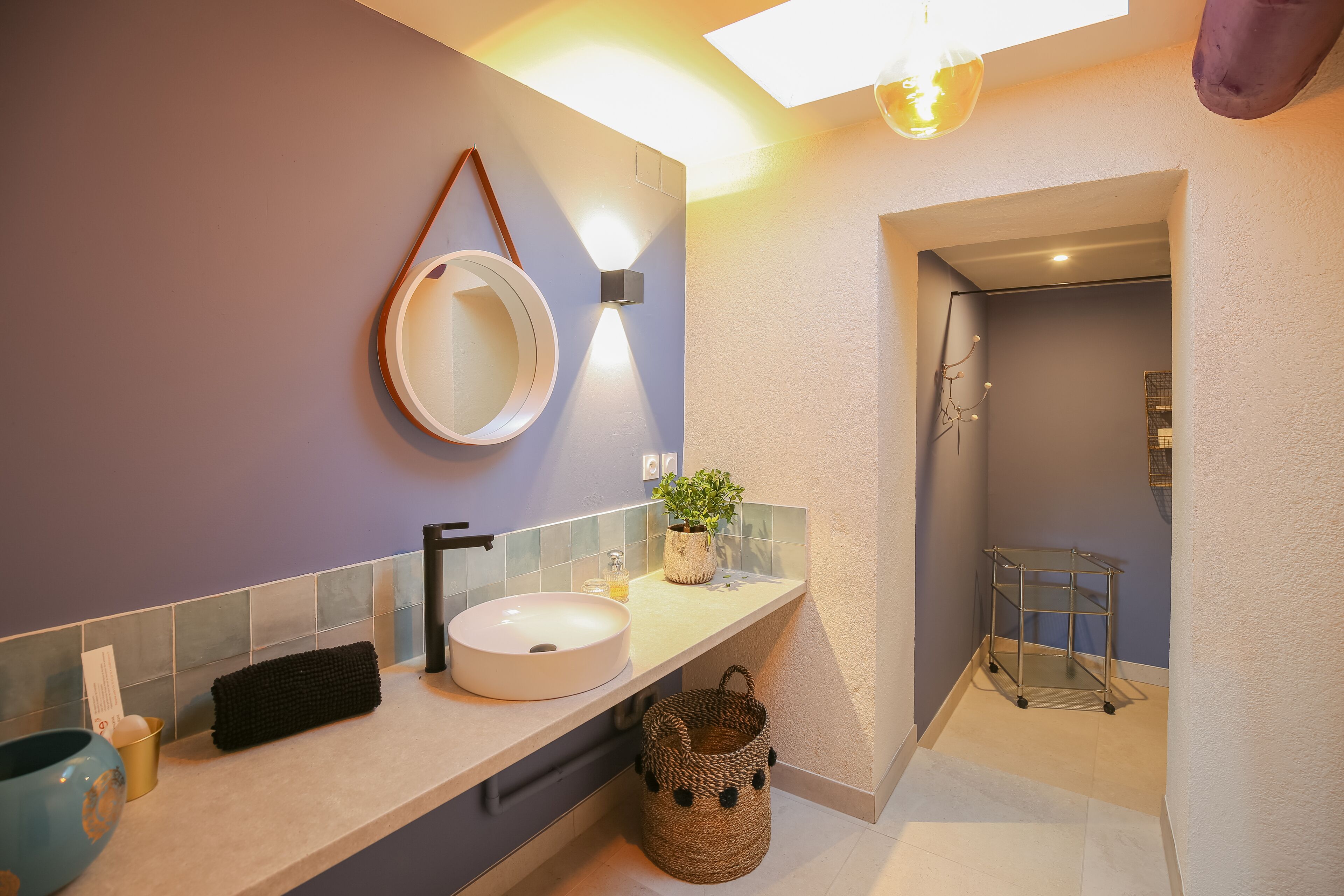 A modern bathroom with a round mirror, a white sink, and a small potted plant on the counter.